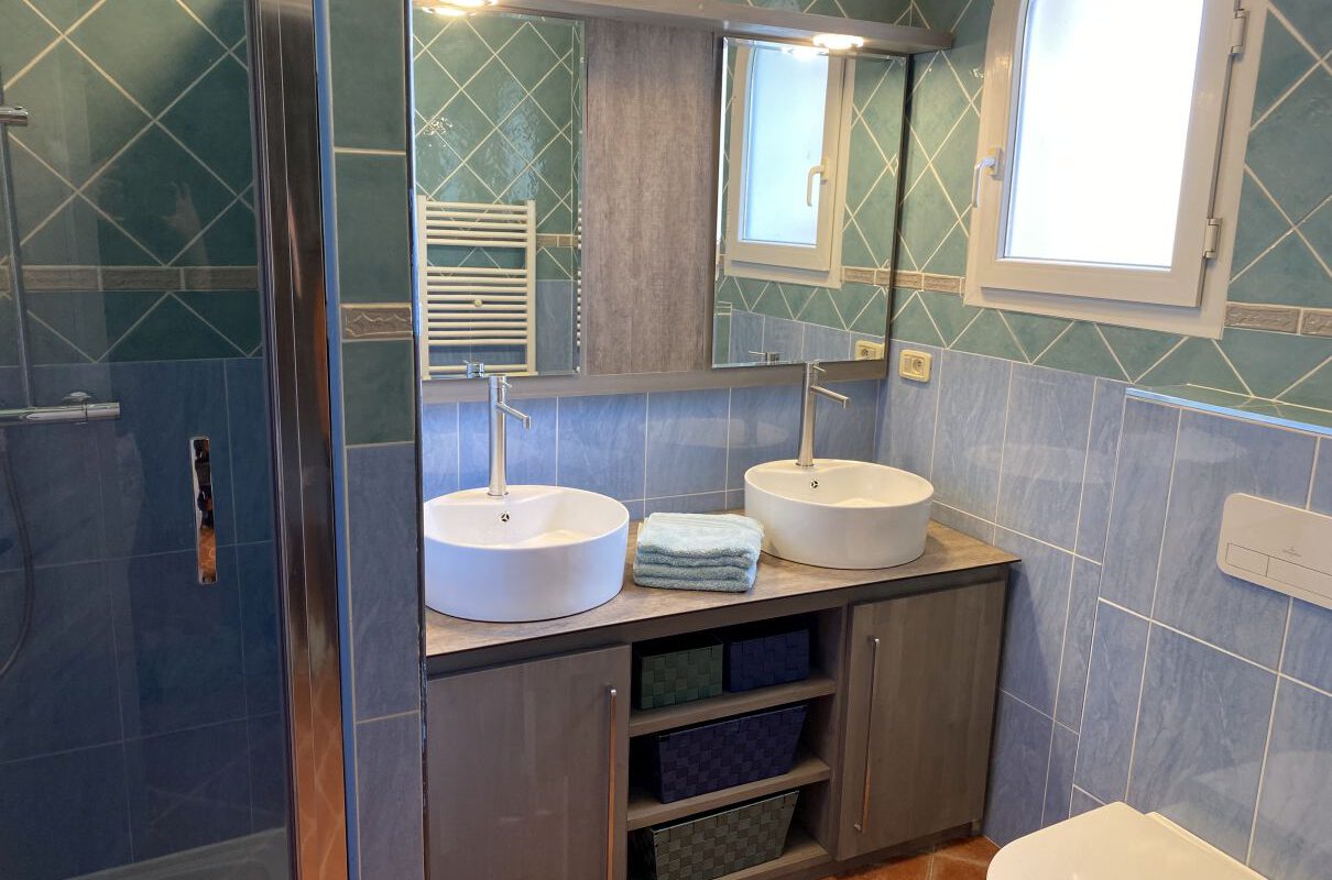 Blaues Badezimmer mit zwei Wasserhähnen und begehbarer Dusche